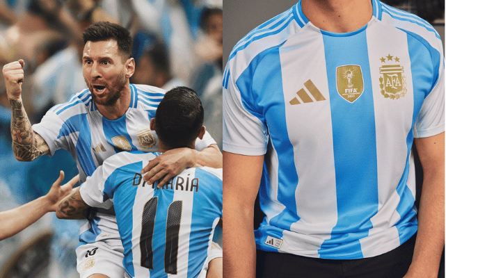 Camisa Titular da Argentina 2024 Adidas Branca e Azul pendurada em um cabide. A camisa é branca com três listras verticais em azul celeste na parte frontal. As mangas também são brancas com listras azuis nas bordas. A gola é redonda com uma faixa branca centralizada na nuca. O logo da Adidas está estampado em dourado no lado direito do peito, enquanto o escudo da AFA está em dourado no lado esquerdo do peito. O patch de campeã mundial está dourado no centro do peito.